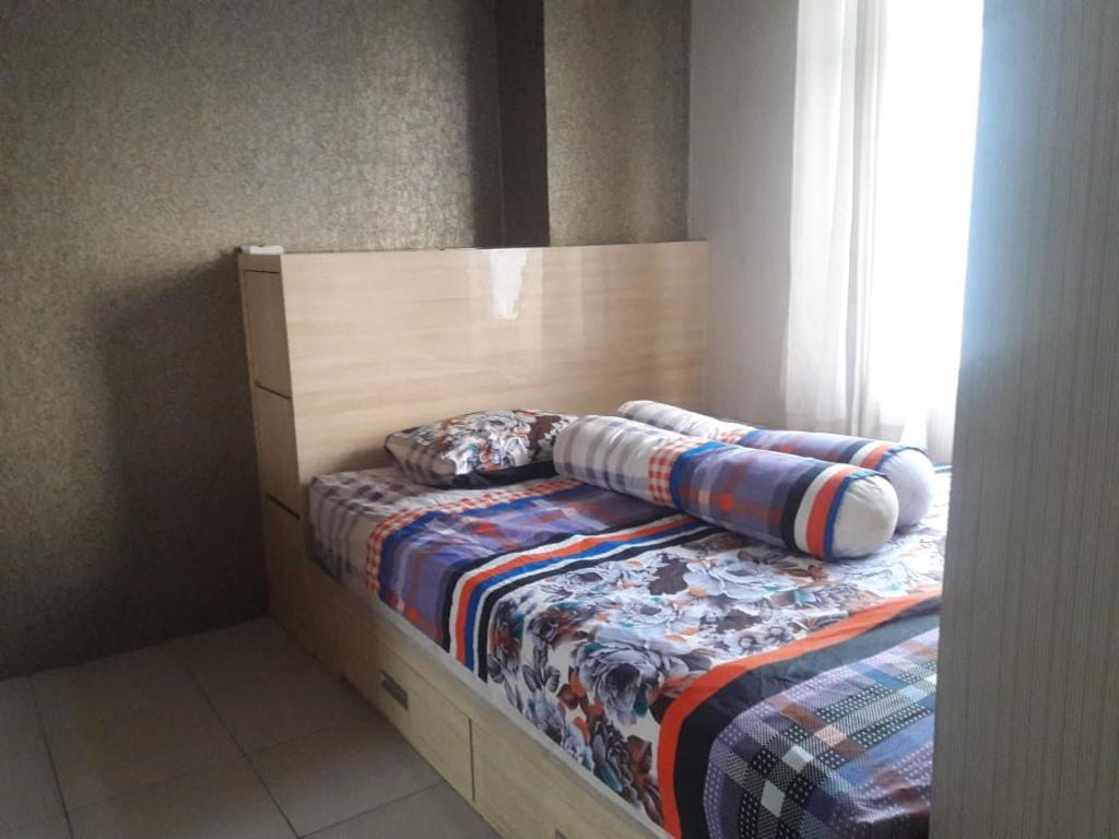 a bed with a wooden headboard and pillows on it at Apt Greenbay Baywalk Mall Pluit Seaside 2 Bedroom with Pool Facility in Jakarta