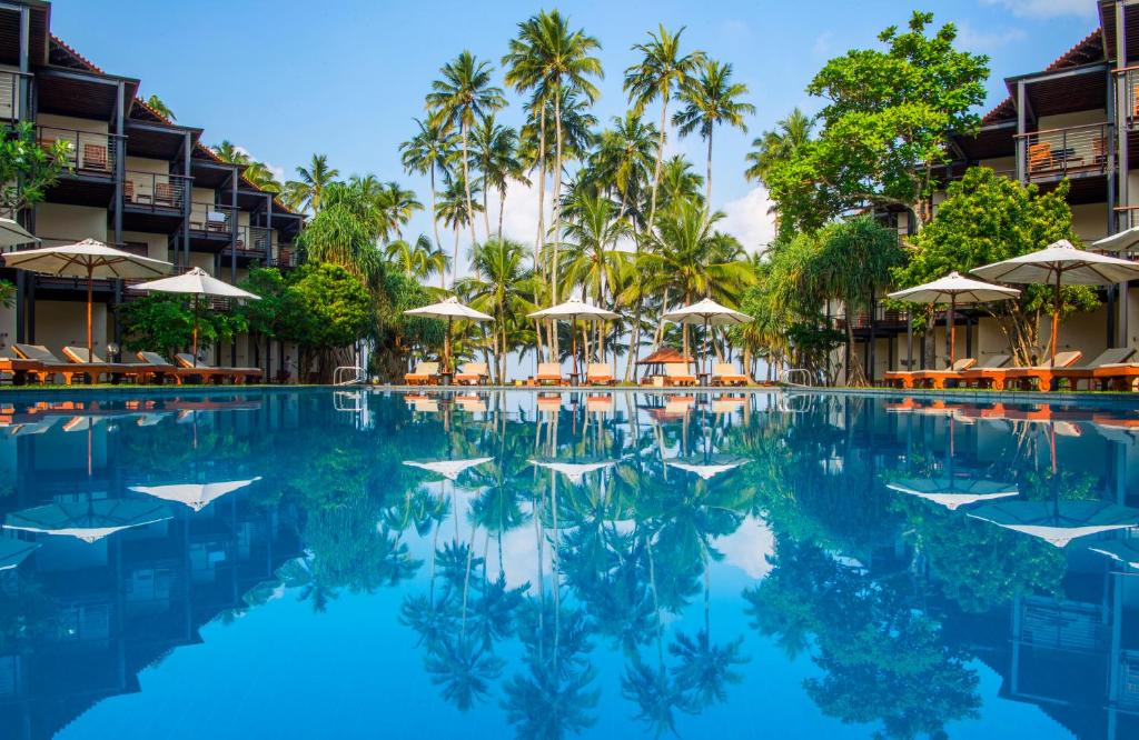 einen Pool in einem Resort mit Palmen und Sonnenschirmen in der Unterkunft Mermaid Hotel & Club in Kalutara