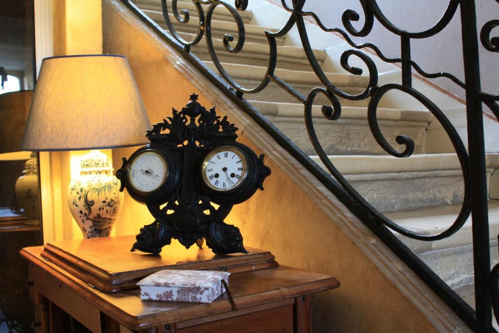 un reloj sentado en una mesa junto a una lámpara en Logis Les Remparts, en Bayeux