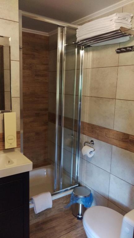 Compact tiled bathroom featuring glass shower, toilet, wall-mounted towel rack with folded towels.