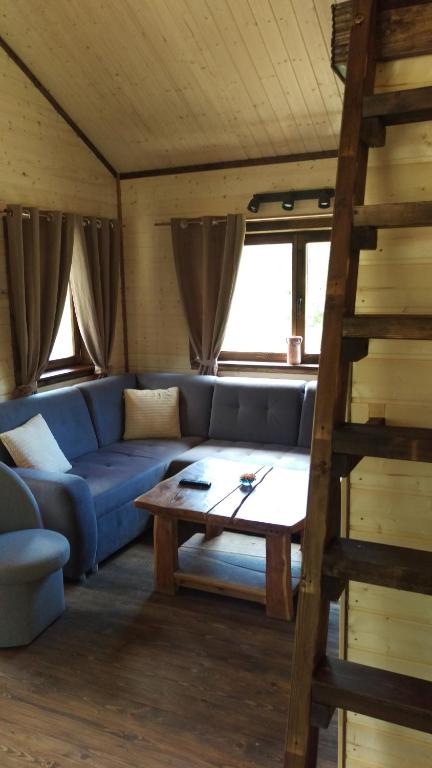 Cozy wooden cabin living area with blue L-shaped sofa, rustic coffee table, ladder to loft.
