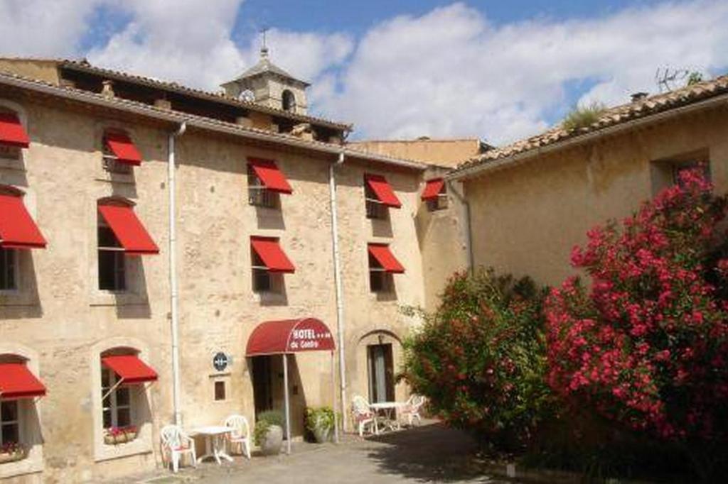 ein Gebäude mit roten Markisen, Tischen und Stühlen in der Unterkunft Hotel du Centre in Pierrelatte