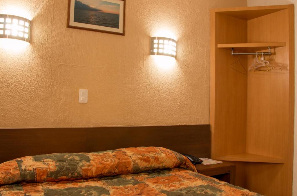 A compact bedroom shows the edge of a double bed beside an open wooden wardrobe.