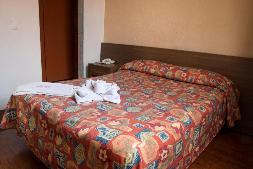 A made double bed is presented with folded towels and a cup arranged on the patterned coverlet.
