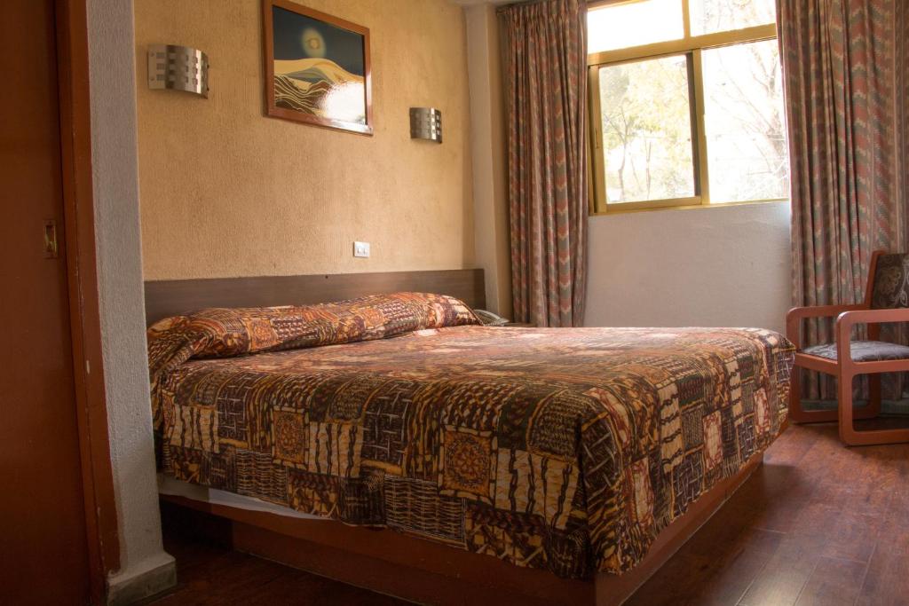 A double room has a bed, patterned textiles, a curtained window and a wooden chair.