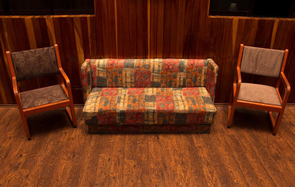 A wood-paneled sitting area with a patterned sofa, two armchairs, and wall-mounted screens.