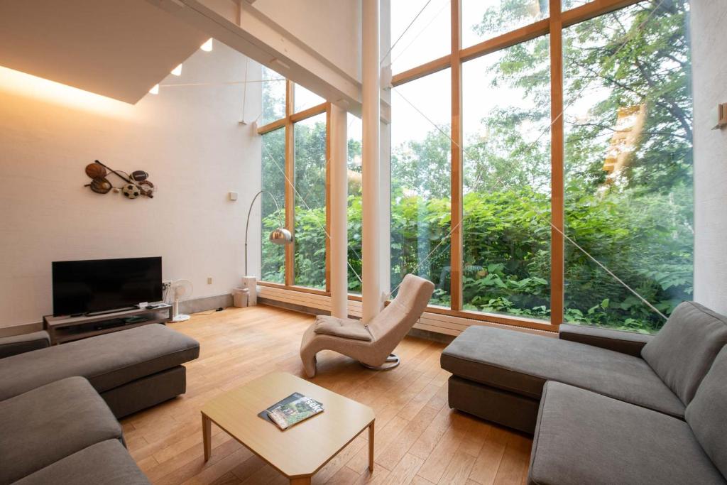 a living room with a couch and a tv and large windows at Sekka House in Niseko