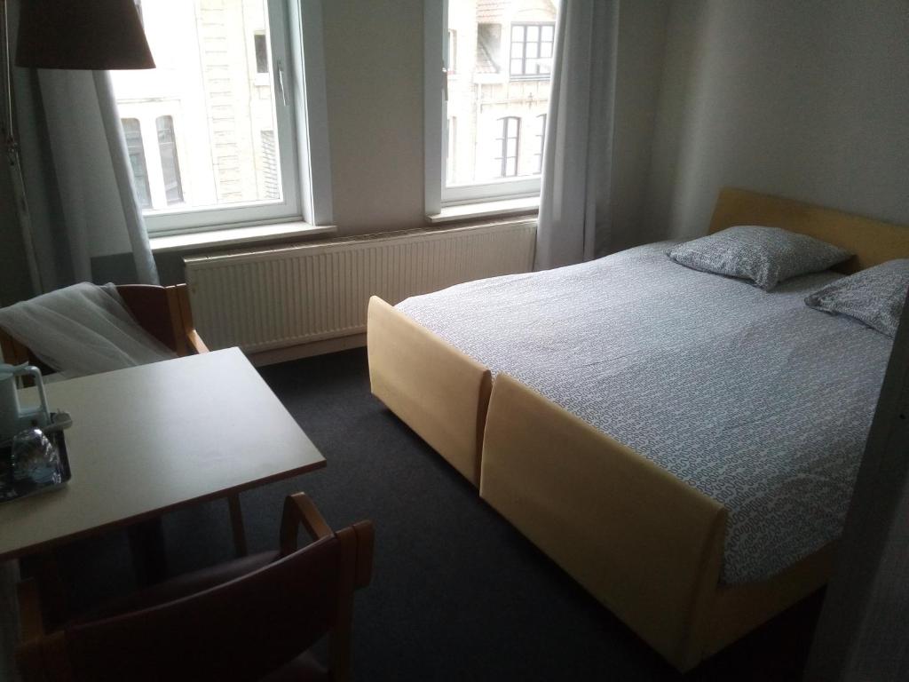 a bedroom with a bed and a table and two windows at Résidence Surmont in Ieper