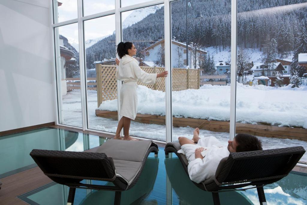 a woman standing in a room looking out a window at a person laying in chairs at Hotel Astoria in Canazei