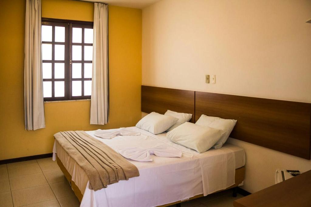 um quarto com uma cama com lençóis brancos e uma janela em Hotel Pousada Trevo em Jequié