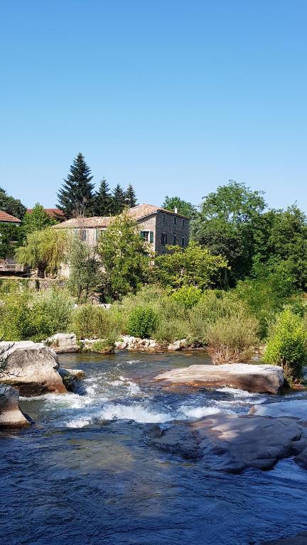 Gite Le Moulin de Rosieres Moulin Champetier في Rosières: نهر فيه صخور ومنزل في الخلف
