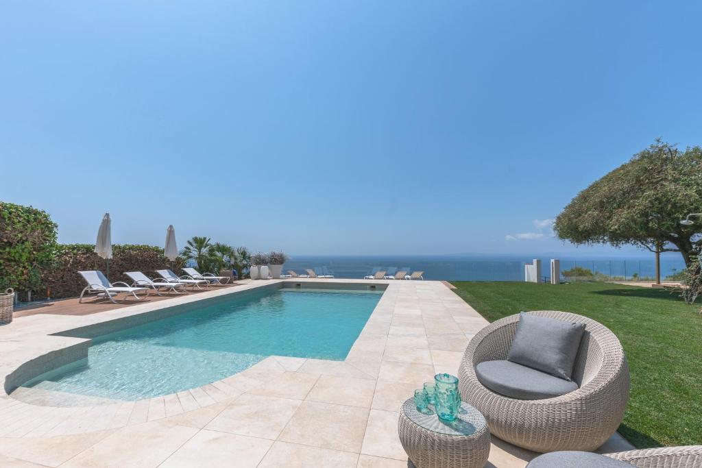 a swimming pool with chairs and the ocean in the background at Villa Luna in Sa Torre