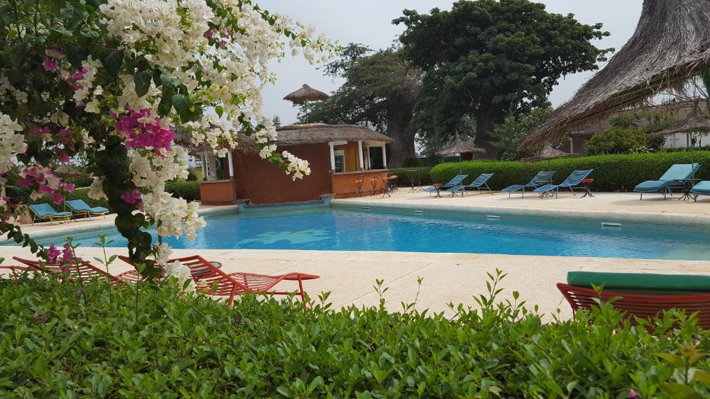 a swimming pool with lawn chairs and flowers at Baobab Soleil in Sindia