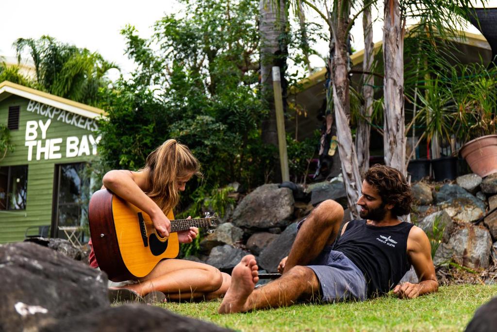 een man en een vrouw op het gras die gitaar spelen bij Backpackers By The Bay in Airlie Beach