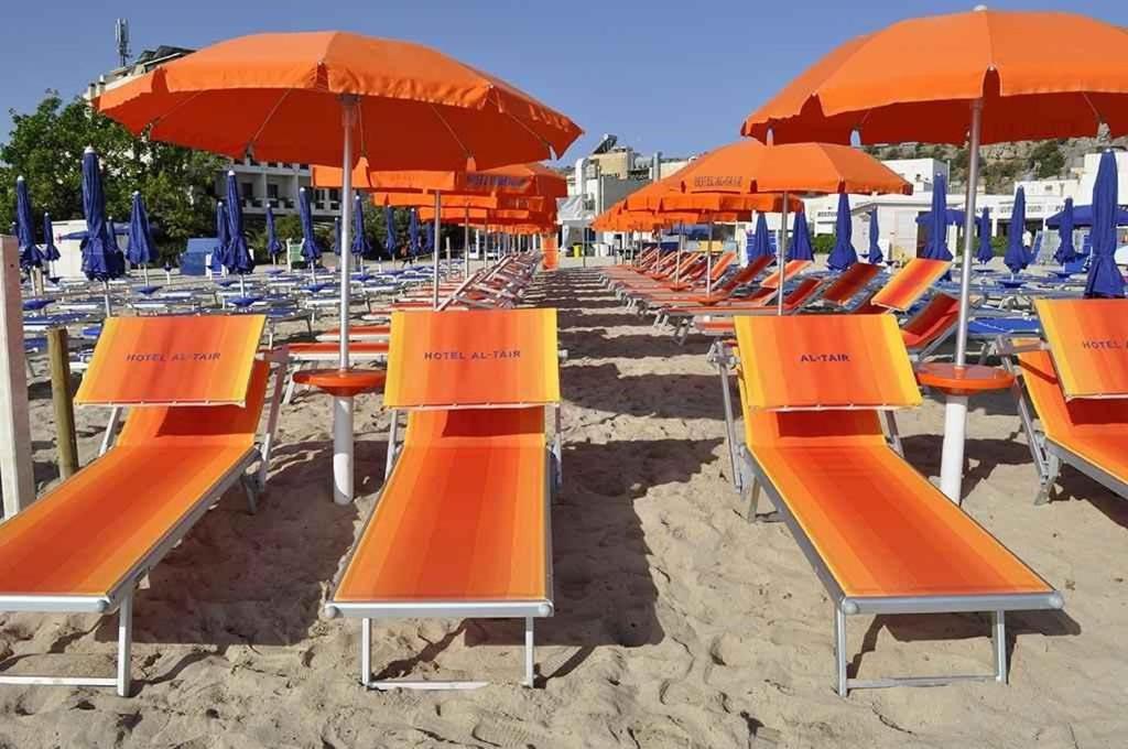 a row of orange chairs and umbrellas on a beach at Al-Tair in San Vito lo Capo