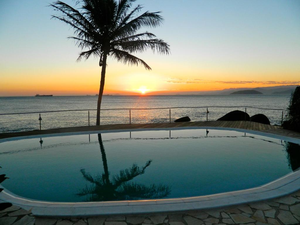 a sunset over the ocean with a swimming pool and a palm tree at Sol-lua Bungalow in Ilhabela