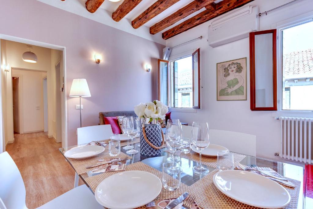 Botteri Palace Apartments في البندقية: غرفة طعام مع طاولة زجاجية وكراسي بيضاء