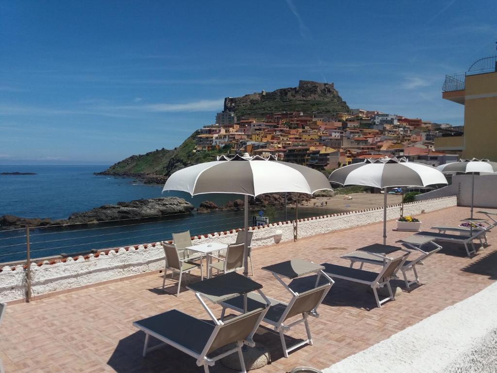 eine Gruppe von Stühlen und Tischen mit Sonnenschirmen und dem Meer in der Unterkunft Hotel Meli in Castelsardo