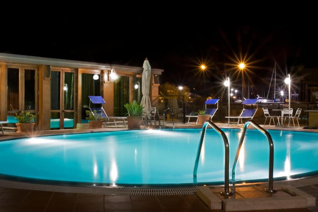 una piscina notturna con sedie e tavoli di David Palace Hotel a Porto San Giorgio