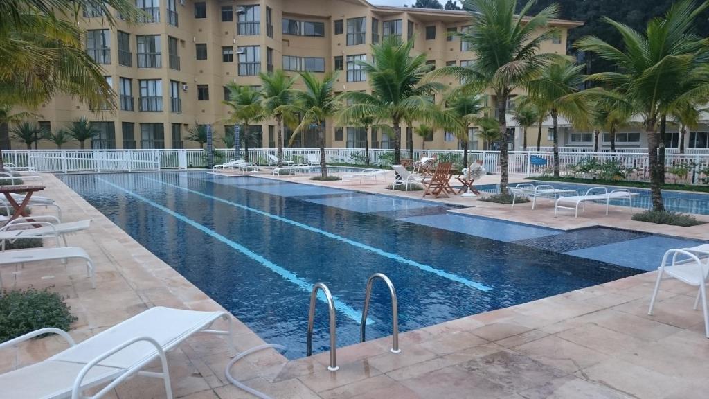 a pool at a hotel with palm trees and buildings at Loft com Praia in Mangaratiba