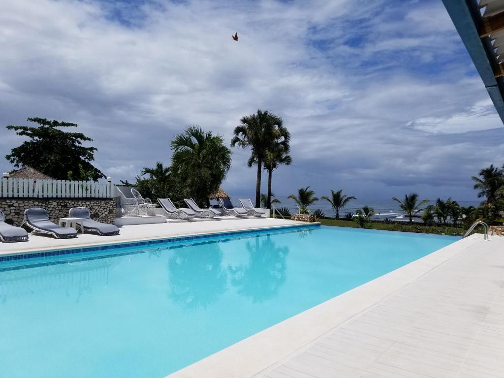 a large swimming pool with chairs and palm trees at Hotel El Quemaito - Luxury Oceanfront Retreat in Santa Cruz de Barahona