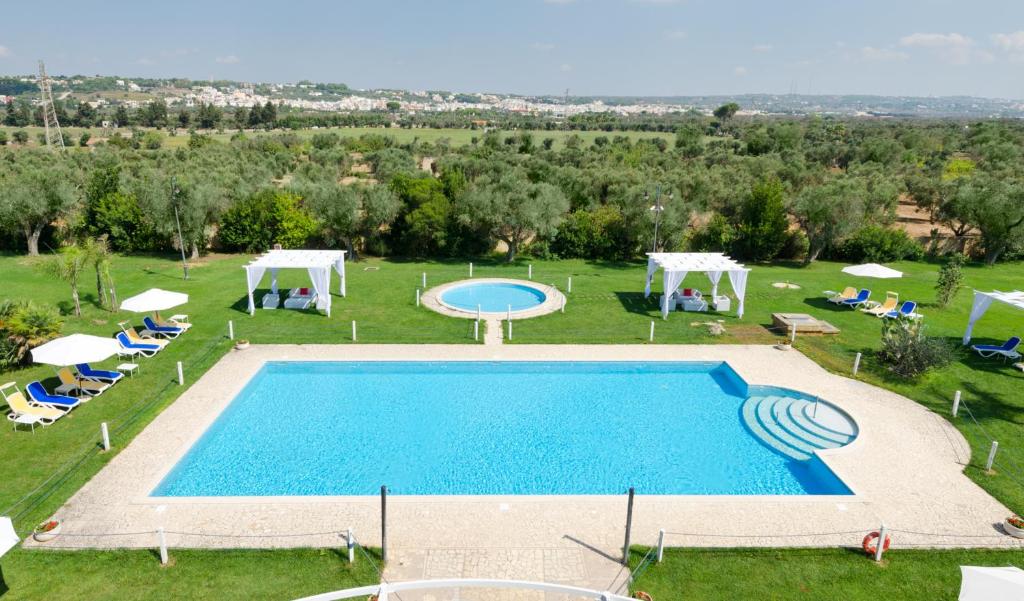 a large swimming pool in a field with chairs and umbrellas at Masseria La Baronessa Resort in Tuglie