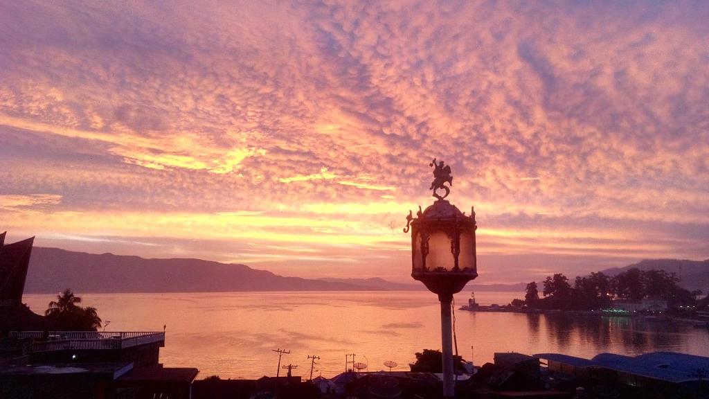 a street light in front of the water with a sunset at Melissa Palace Hotel and Karaoke in Parapat