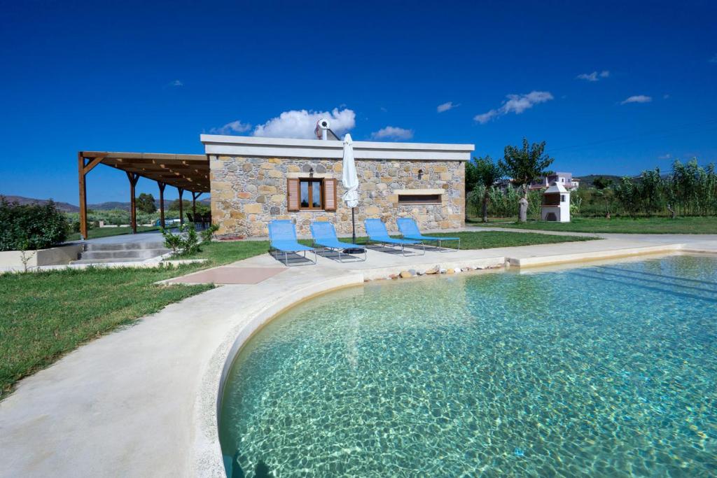 a pool in front of a stone house with blue chairs at Iridanos Villa in Kissamos