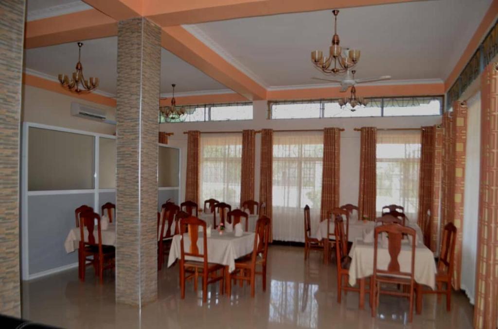 a dining room with tables and chairs and windows at Cashewnut Hotel in Mtwara