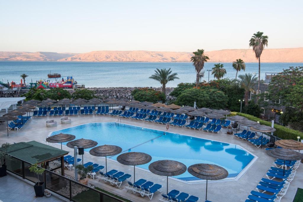 a beach with a pool, chairs, tables and umbrellas at Leonardo Plaza Hotel Tiberias in Tiberias