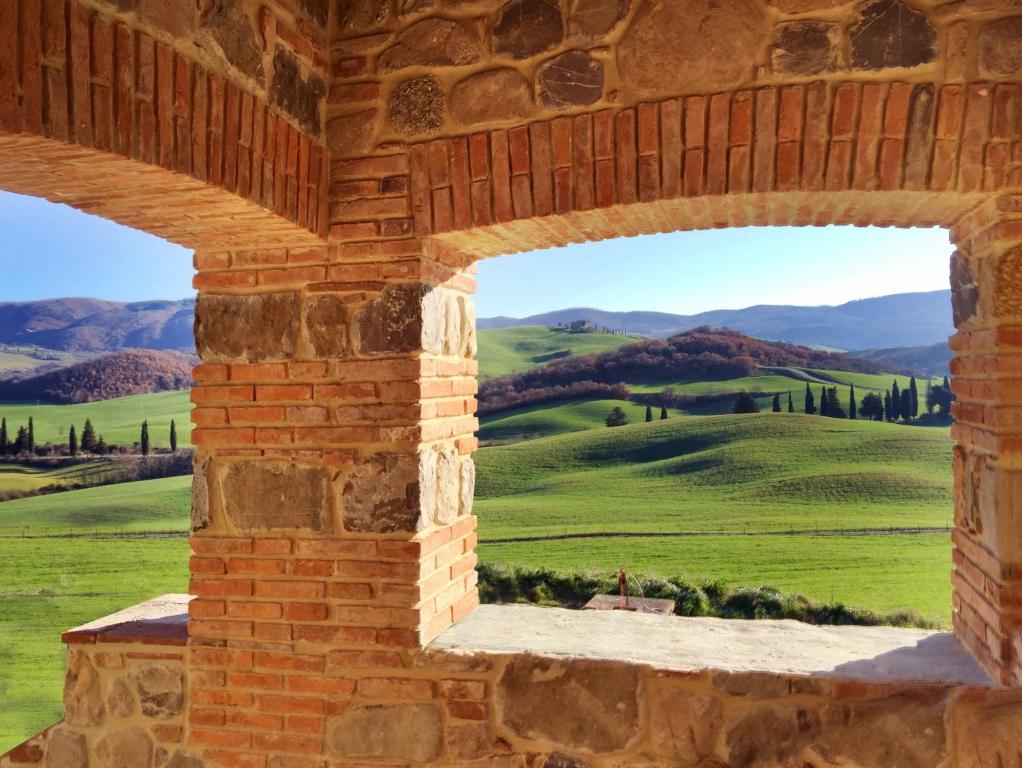 ein Fenster in einer Ziegelmauer mit Blick auf ein grünes Feld in der Unterkunft RELAIS VAL D'ORCIA in Pienza