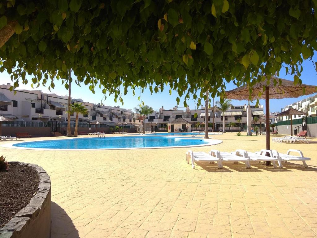 een zwembad met twee witte stoelen en een parasol bij Residencial Los Geranios 13 in Costa Del Silencio