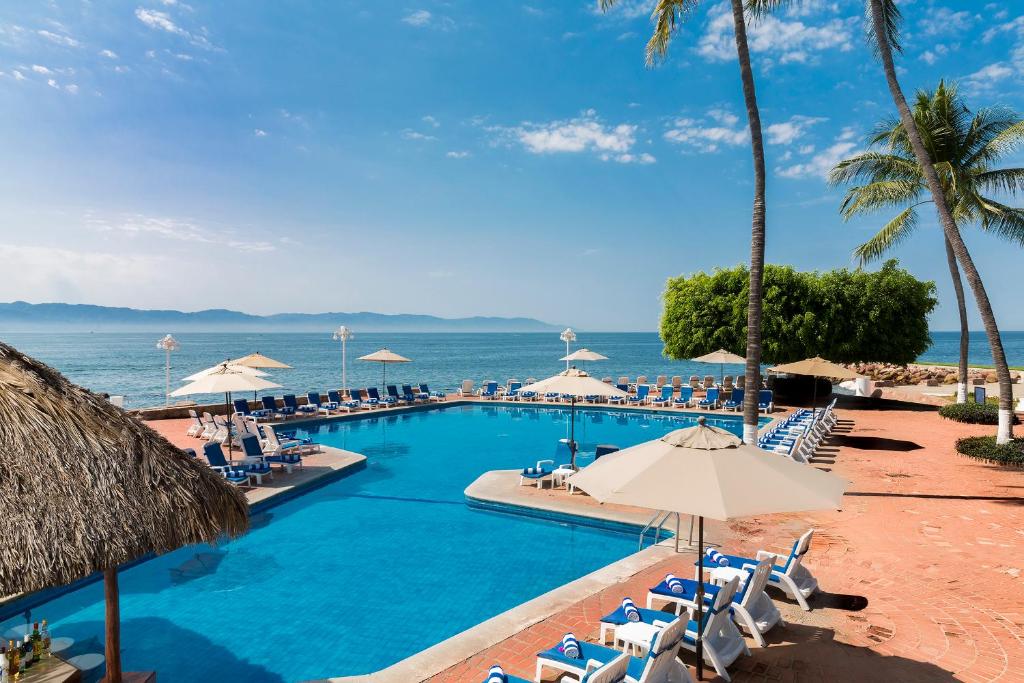 uma piscina com cadeiras e guarda-sóis e o oceano em Vamar Vallarta Marina & Beach Resort em Puerto Vallarta