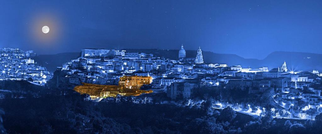 una vista di una città di notte con la luna di San Giorgio Palace Hotel Ragusa Ibla a Ragusa