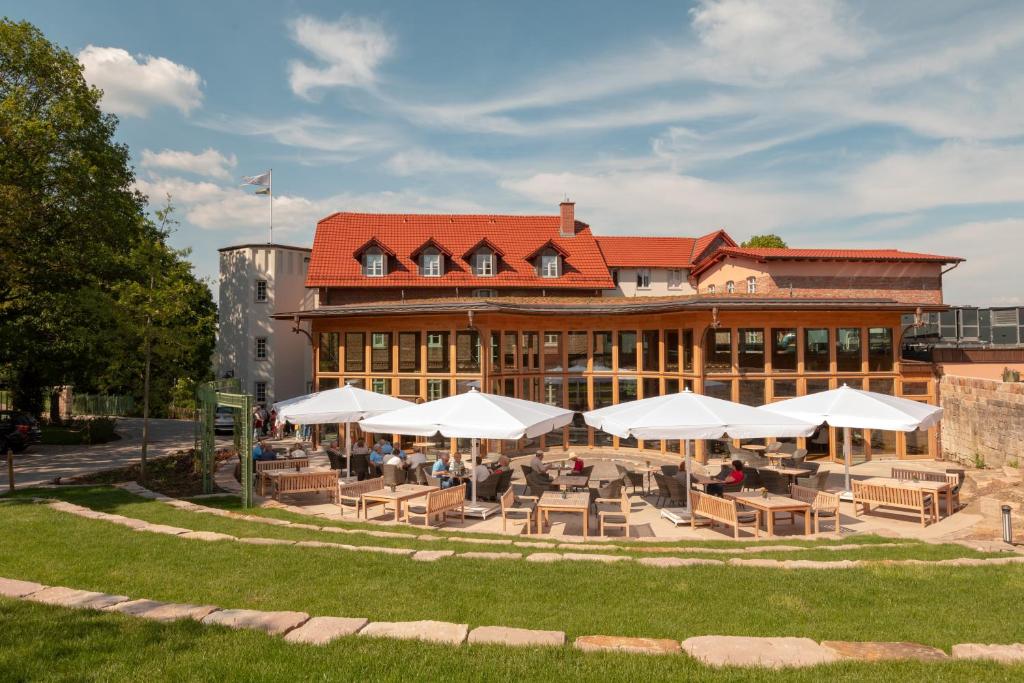 un edificio con mesas y sombrillas blancas delante de él en Hotel Brunnenhaus Schloss Landau, en Bad Arolsen