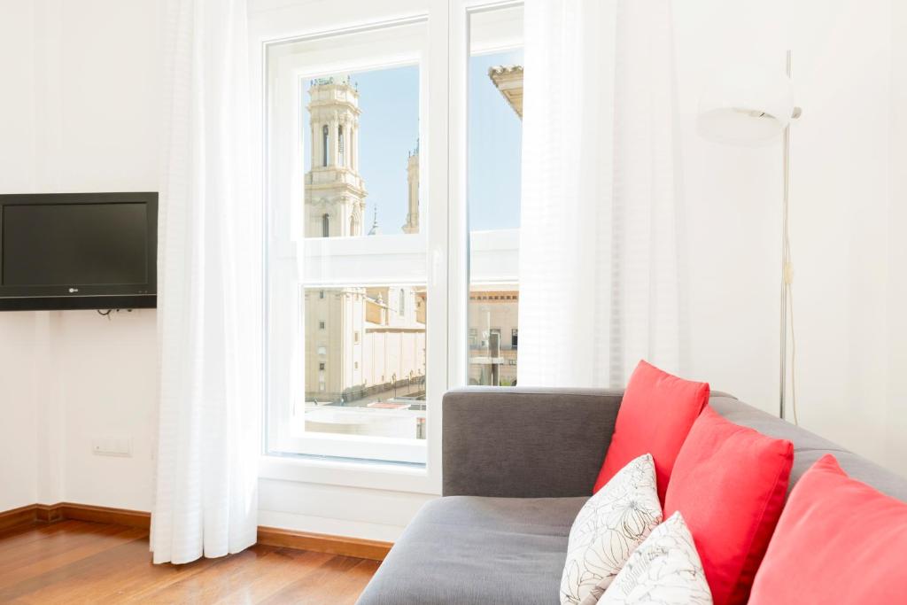 a living room with a couch and a large window at Apartamentos Sabinas El Pilar in Zaragoza