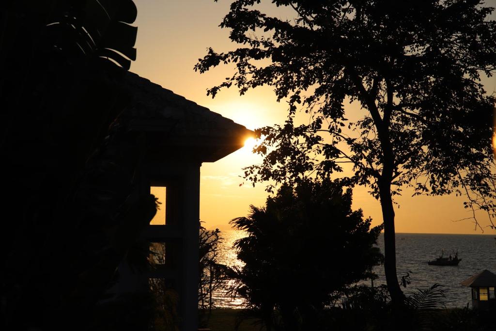 un coucher de soleil sur l'océan avec une maison et un arbre dans l'établissement Baan Dhewaran Beachfront Villa, à Na Jomtien