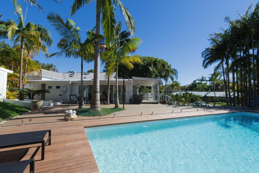 a swimming pool in front of a house with palm trees at Byron Springs in Byron Bay