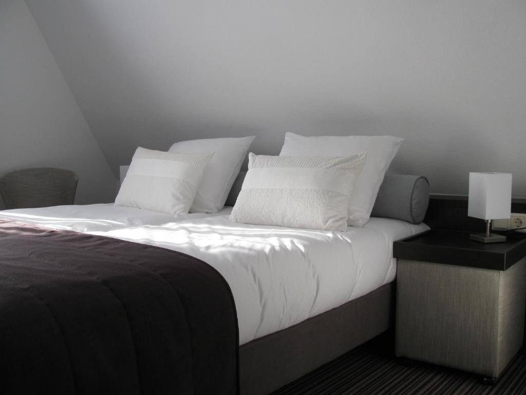 a bedroom with a bed with white pillows and a lamp at Boutique Hotel de Zwaluw in De Koog