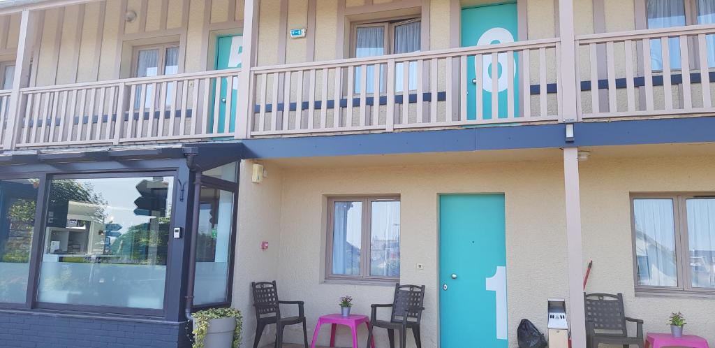 a building with a balcony with a blue door and chairs at Hôtel L'ideal le Mountbatten in Arromanches-les-Bains