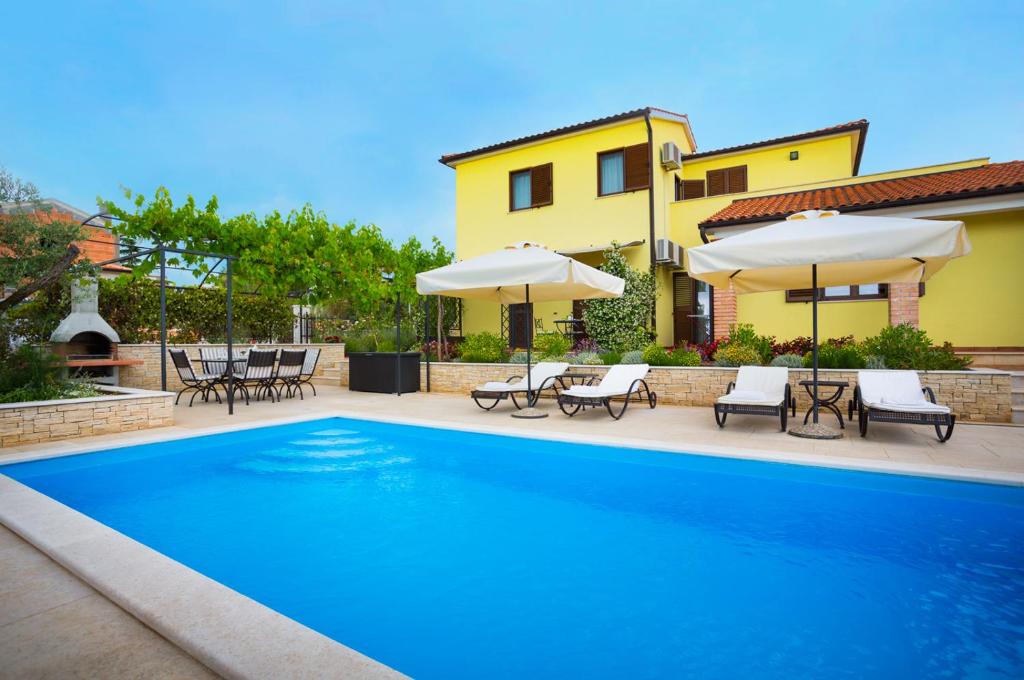 a swimming pool with chairs and umbrellas next to a house at Apartmani Hrelja in Labinci