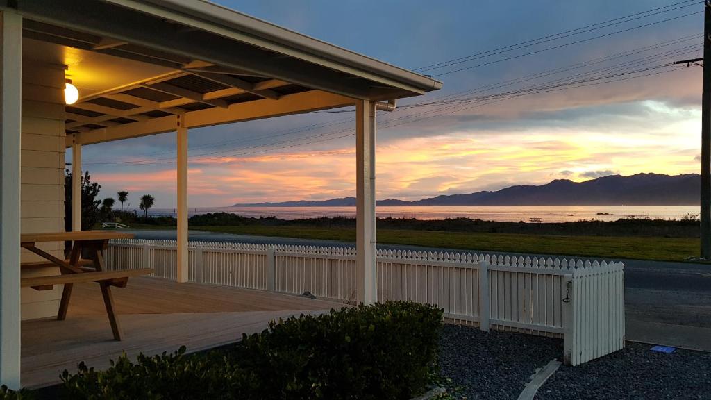 a house with a wooden deck with a sunset at K'orca Cottage by the Sea in Kaikoura