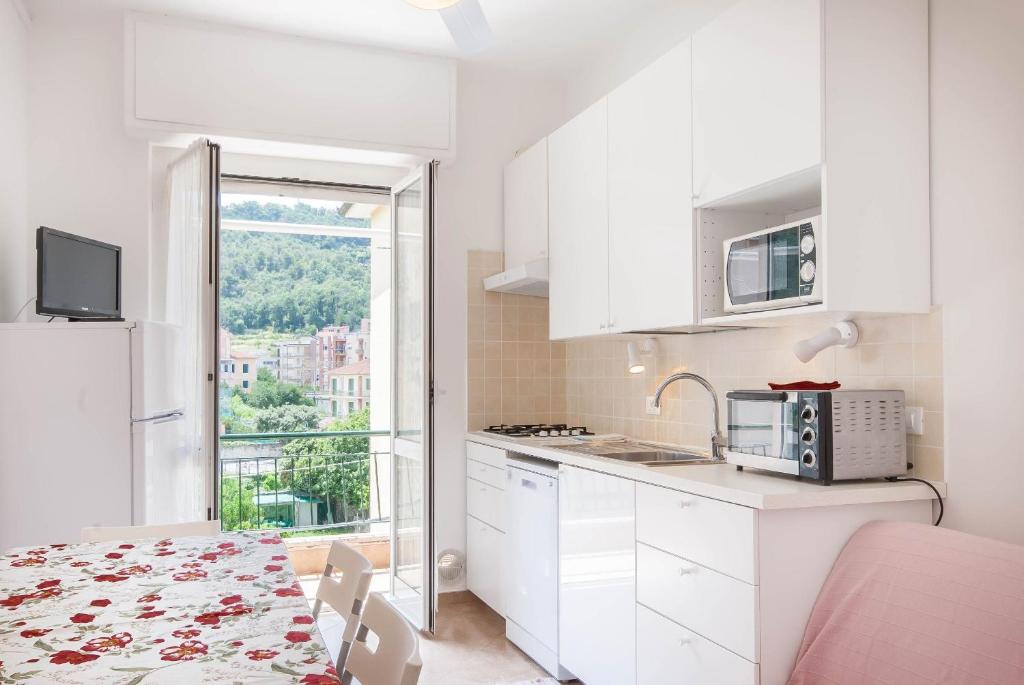 cocina con armarios blancos, mesa y ventana en Appartamenti family & MTB, en Finale Ligure