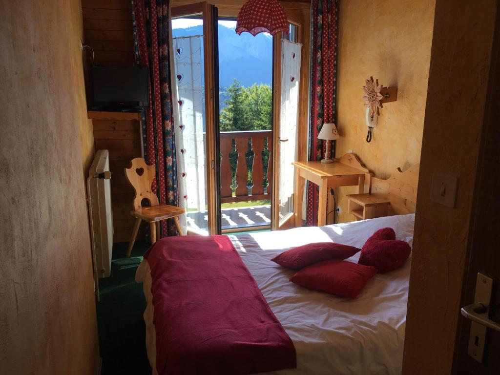 una camera da letto con balcone e letto con cuscini rossi. di Hôtel les skieurs a Bellevaux