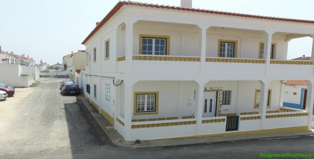 a white building with a car parked in a parking lot at Hostel Nature in Zambujeira do Mar