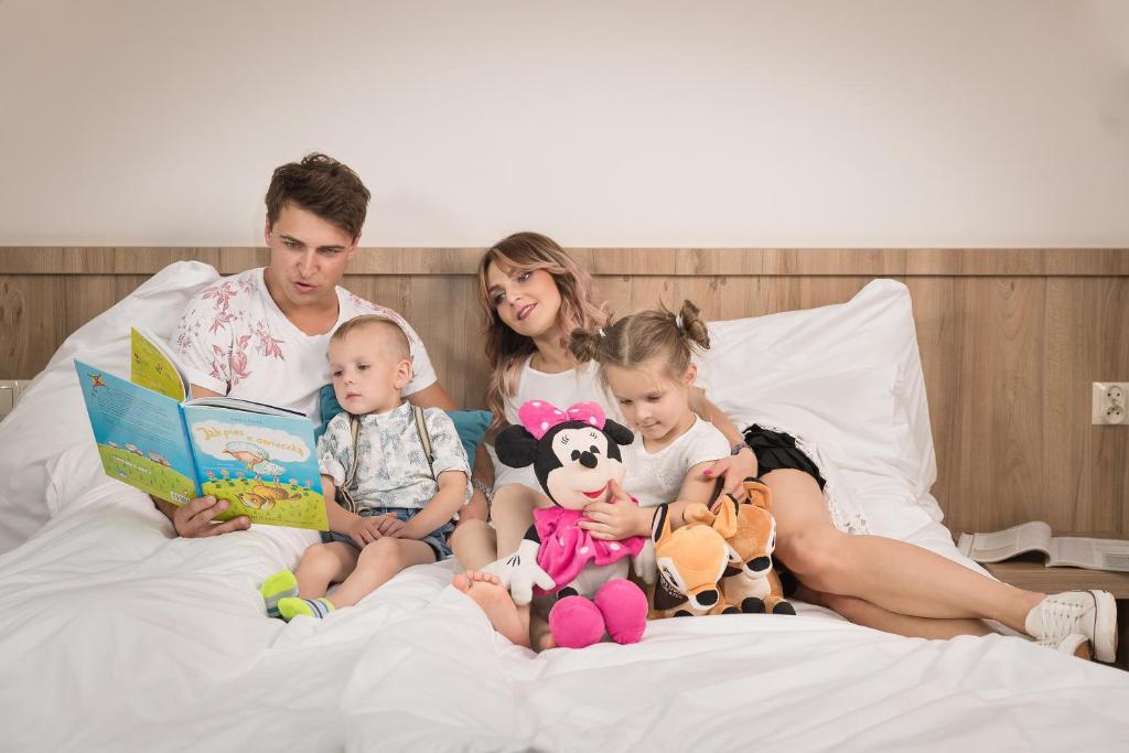 Borowy Dwór- Biznes, Spa & Fun في شافلاري: رجل وثلاث اطفال جالسين على سرير يقرؤون الكتب