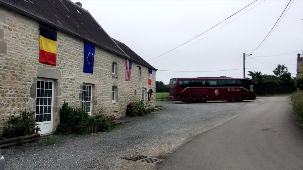 un autobús rojo estacionado al lado de un edificio con una bandera en chevrerie de la huberdiere, en Liesville-sur-Douve