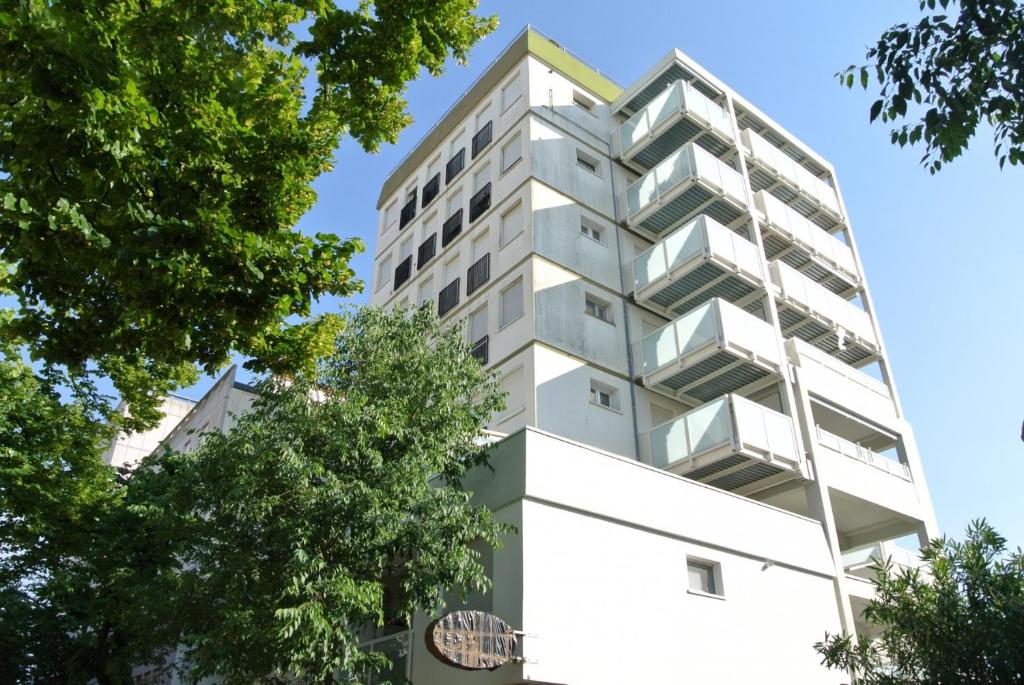 a tall white building with trees in front of it at Appartamento CRISTALLO 25 in Lignano Sabbiadoro
