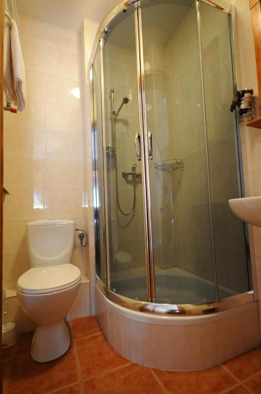Compact bathroom with curved glass shower enclosure, white toilet, sink, warm tiled floor.