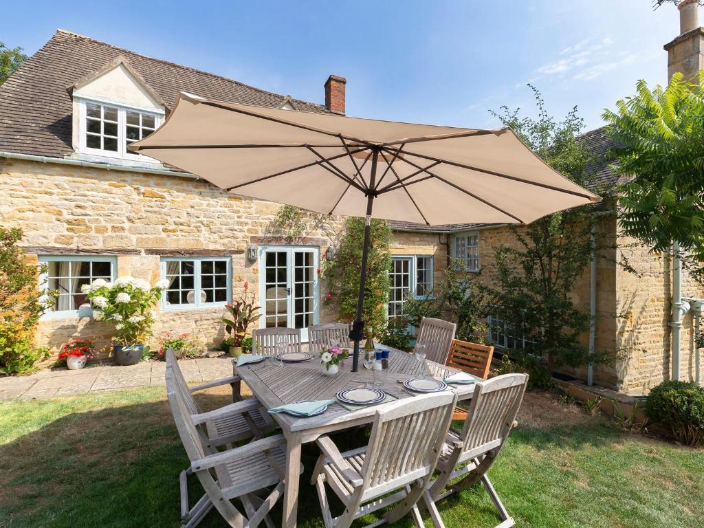 a wooden table with an umbrella in front of a house at Pilgrim Cottage in Bourton on the Hill